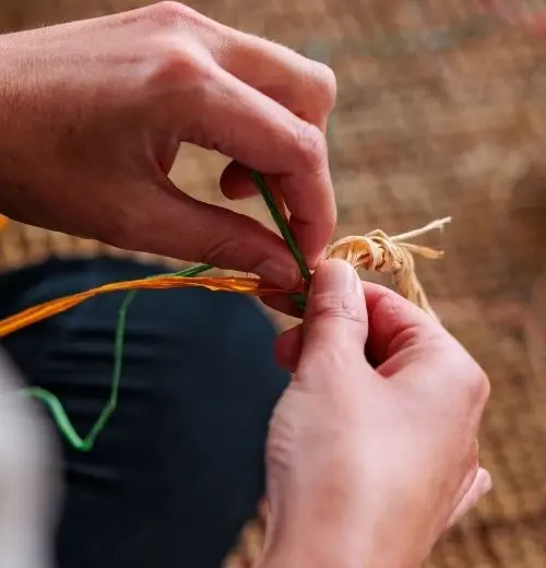 Two hands weaving threads.