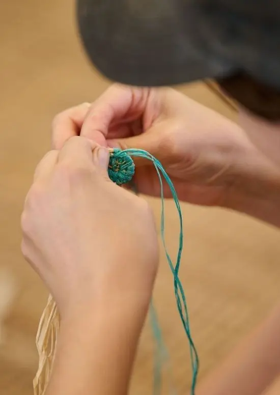 Person weaving blue and yellow natural threads.