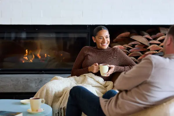 Two people with hot chocolate in front of a fireplace.