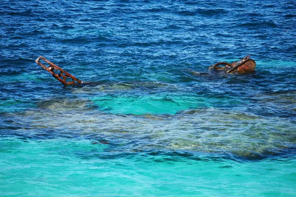 The remains of a shipwreck partially submerged in clear blue ocean water, with rusted metal visible above the surface.