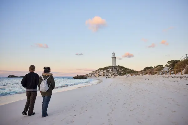 A couple walking on the beach towards a lighthouse