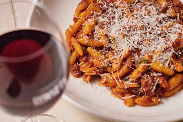 A bowl of pasta with a glass of pinot.