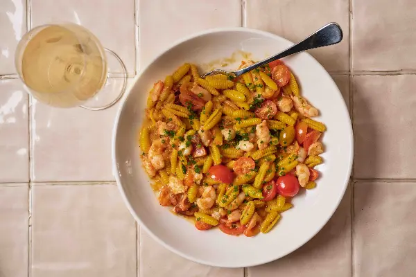 A bowl of prawn pasta with a glass of pinot.