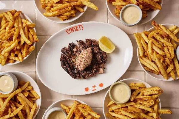 A plate of steak with bowls of hot chips and sauce.