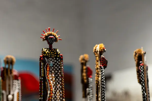 A series of Aboriginal wood statues up close with dot-painted bodies and textured, grassy hair.