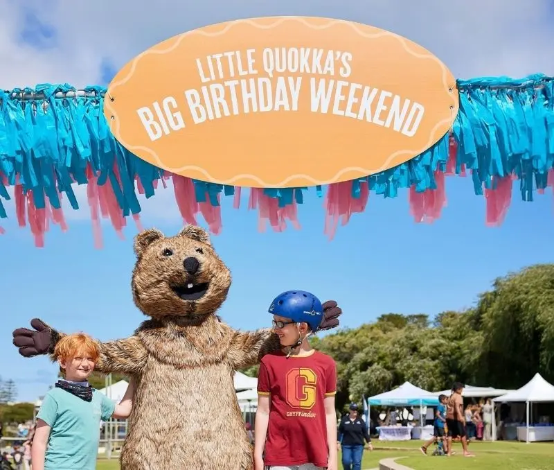 Picture of two children and a Quokka mascot underneath a "Little Quokka's Big Birthday Weekend" sign.