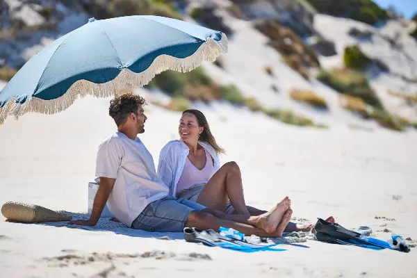 Couple sitting on the beach under an umbrella looking at each other smiling