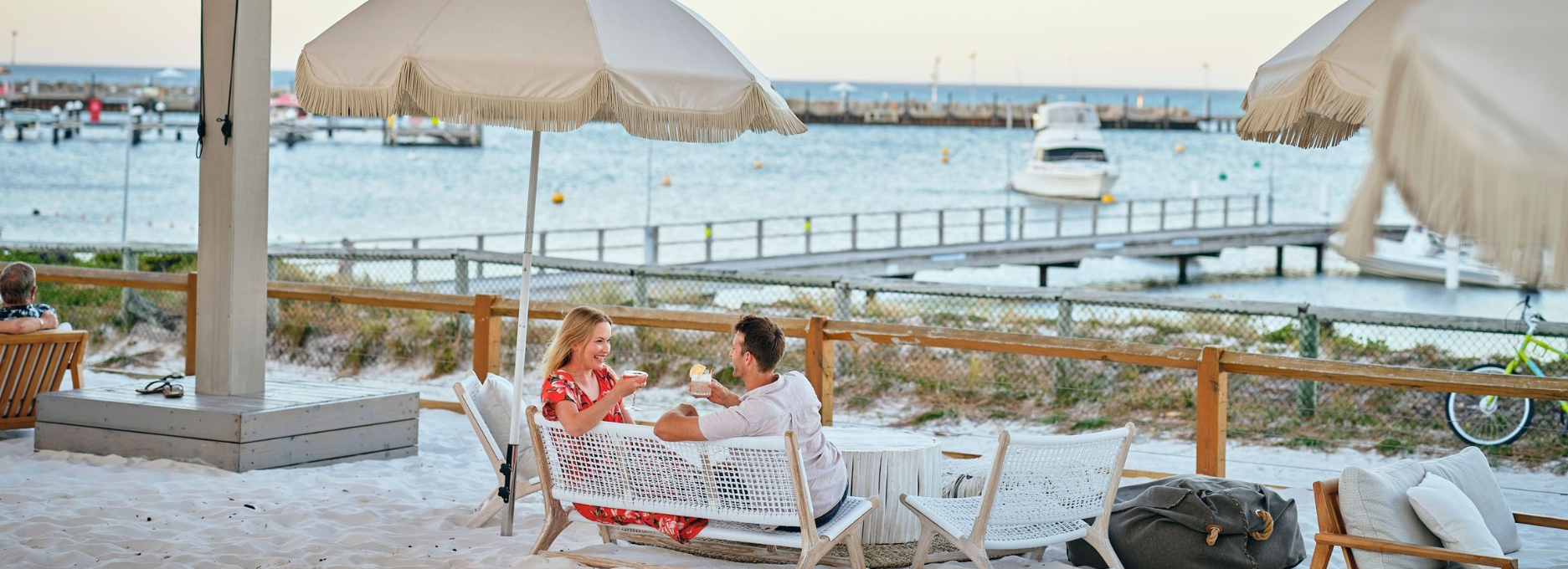 Couple looking at each other smiling sitting under an umbrella in the evening having a drink with views of Thomson Bay