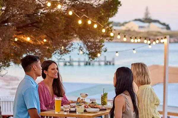 A group of friends having dinner by the water with festoon lights overhead