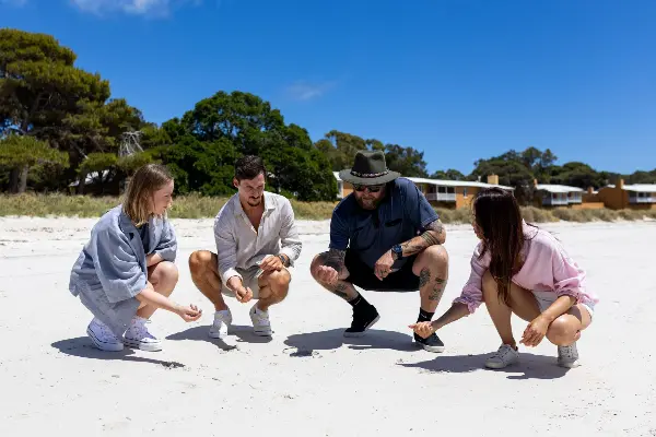 Group of people crouching down and holding sand from the beach in one hand