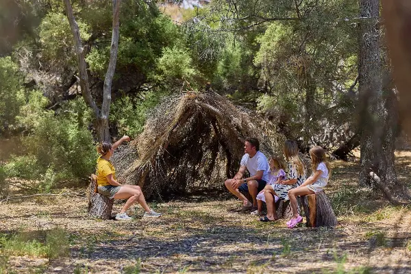 Family sitting looking at a shelter built by branches surrounded by trees