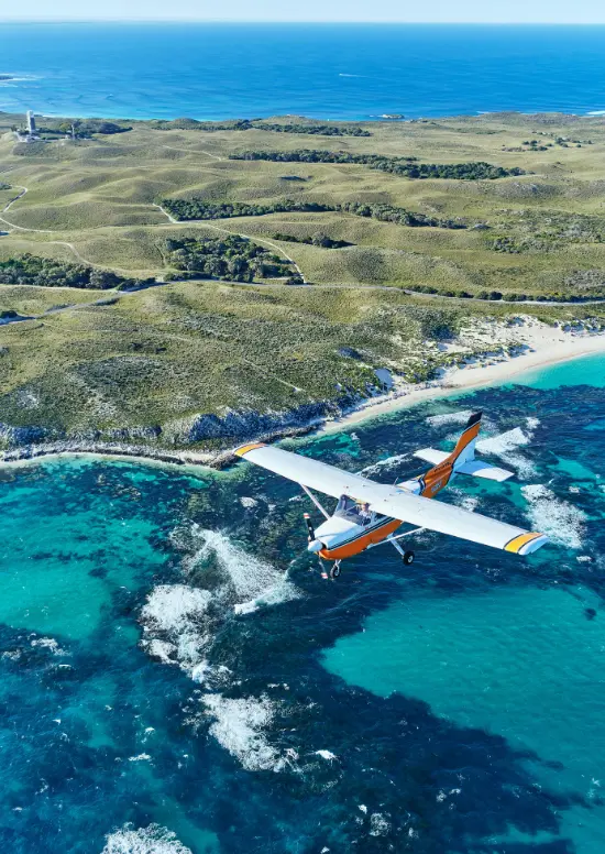 A small white and orange plane flying over Rottnest Island
