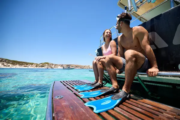 A man and woman sat on the back of a boat wearing flippers on their feet.