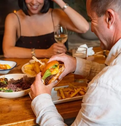 A man holding a burger surrounded by friends.