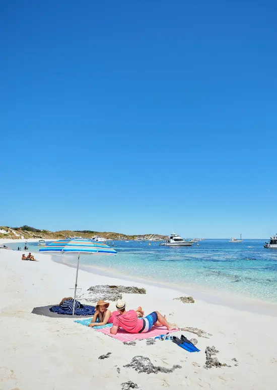 Couple sitting under a beach umbrella with bright blue ocean and white sand