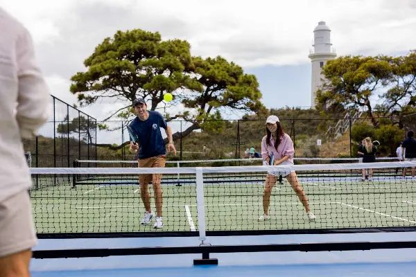 People playing pickleball on courts with lighthouse in background