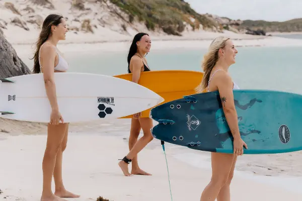 Three girls carrying surfboards to the sea on Rottnest Island