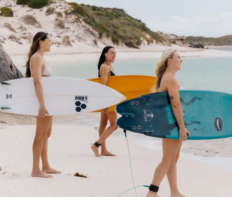 Three girls carrying surfboards to the sea on Rottnest Island