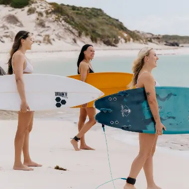 Three girls carrying surfboards to the sea on Rottnest Island