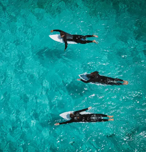Three surfers paddling out into the waves in crystal blue waters